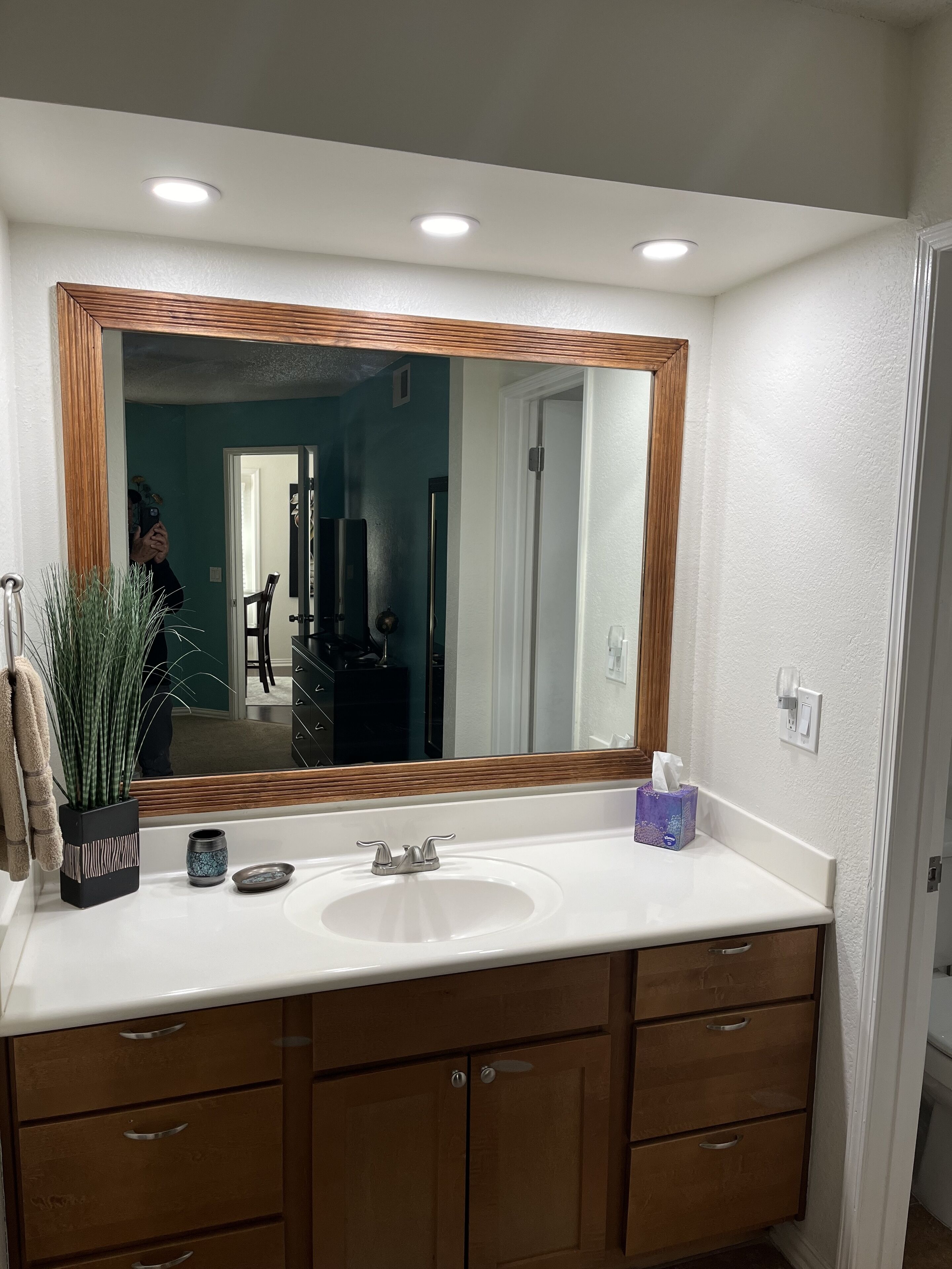 A bathroom with a white sink, wooden cabinets, a large mirror, and a potted plant.
