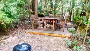 A wooden table and chairs set in a forested area with a barbecue grill in the foreground. - Dog-Friendly, Secluded Redwoods Getaway With Private Hot Tub (Sea Ranch)