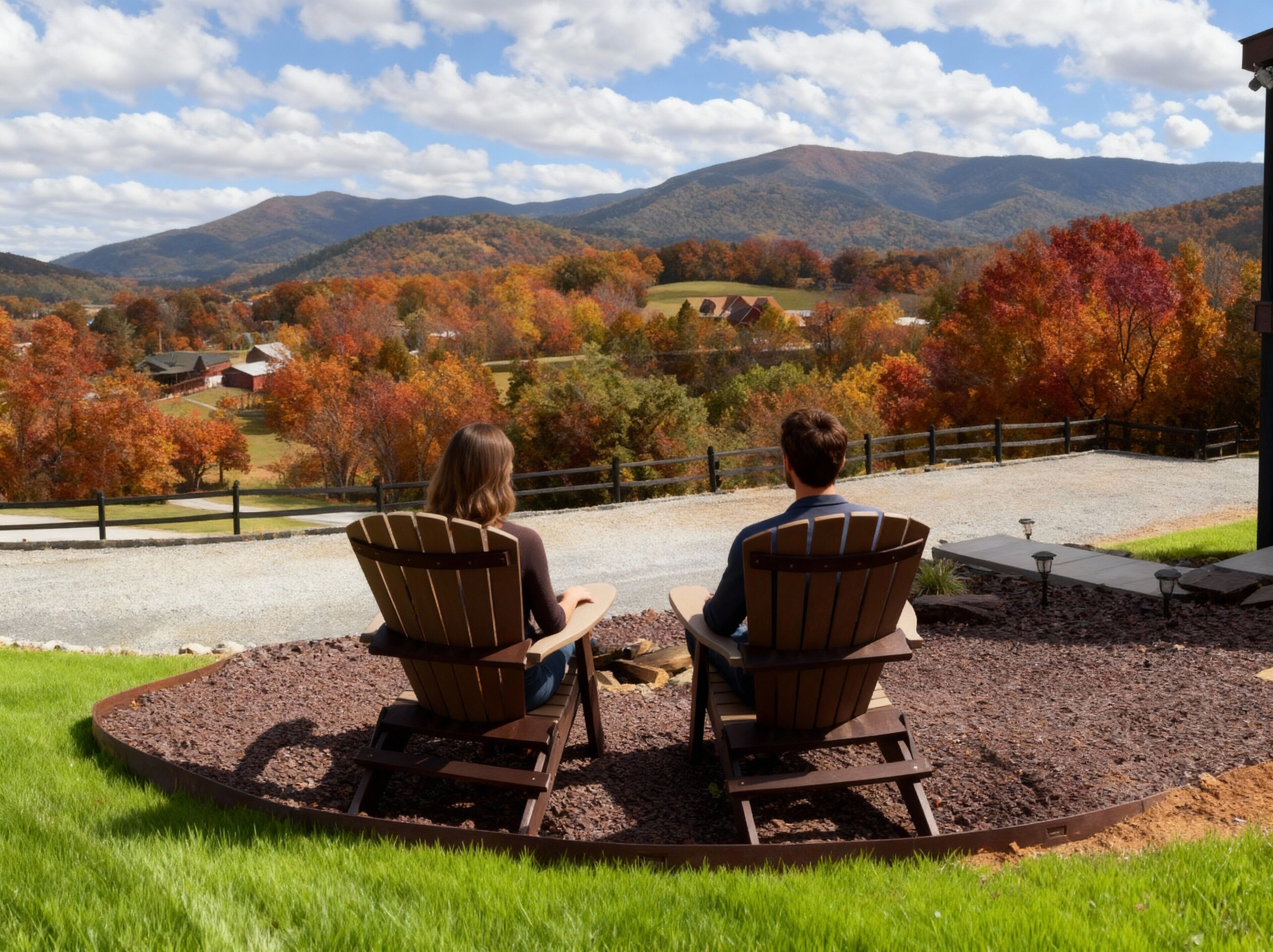 Dos personas sentadas en sillas Adirondack mirando una vista panorámica de un valle con follaje otoñal y montañas distantes.