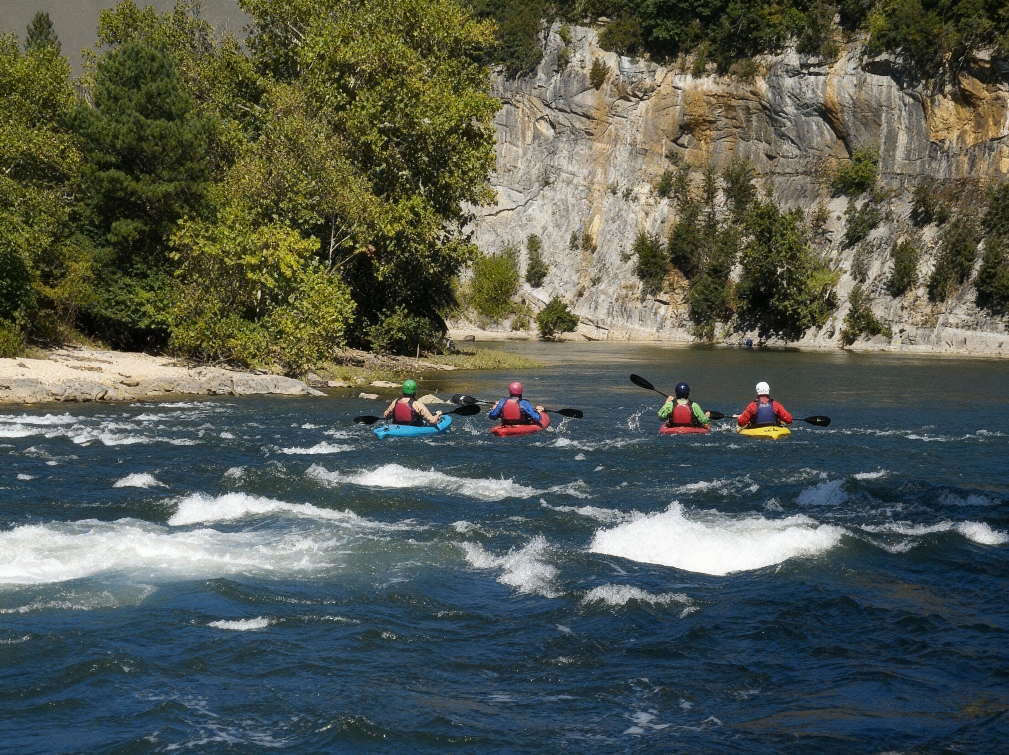 A group of kayakers on a river with rocky cliffs in the background.