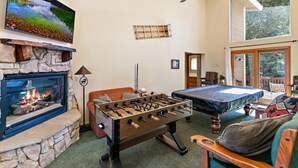 Ein gemütlicher Raum mit Kamin, Fußballtisch, Bett und Wandfernseher.