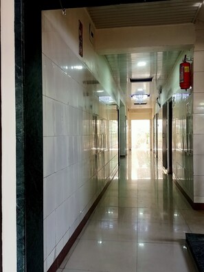 A long, narrow hallway with tiled walls and a shiny floor, leading to a bright exit. - Hotel Geetanjali St Bus Stand Panvel (Panvel)