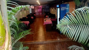 Un restaurante con suelo de madera, mesas con manteles rosa y decoración con plantas tropicales.