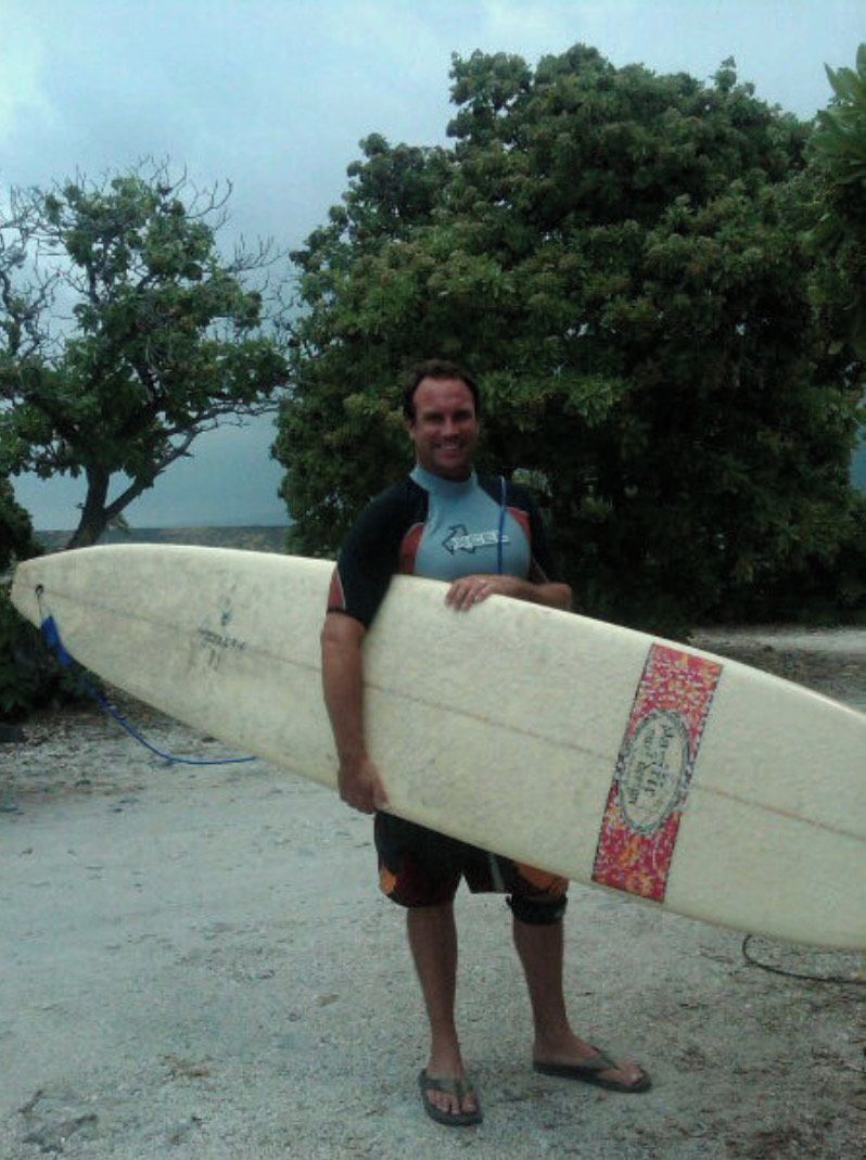 A person holding a surfboard on a sandy beach with trees in the background.