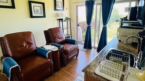 A living room with two brown leather sofas, a kitchen area with a sink and countertop, and a ceiling fan. - Enjoy viewing the photos of your Hale - home away from home (Waikoloa Village)