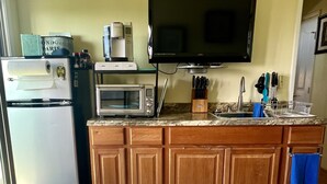 Una cocina equipada con refrigerador, microondas, cafetera y televisor de pantalla plana montado en la pared.