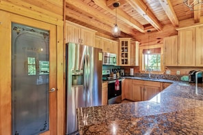 Una cocina con armarios de madera, electrodomésticos de acero inoxidable, encimeras de granito y techo de madera.