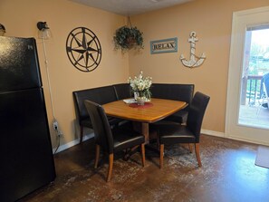 Un comedor con una mesa de madera, sillas negras, un refrigerador negro, una brújula montada en la pared, un letrero que dice 'RELAX' y una planta colgante.
