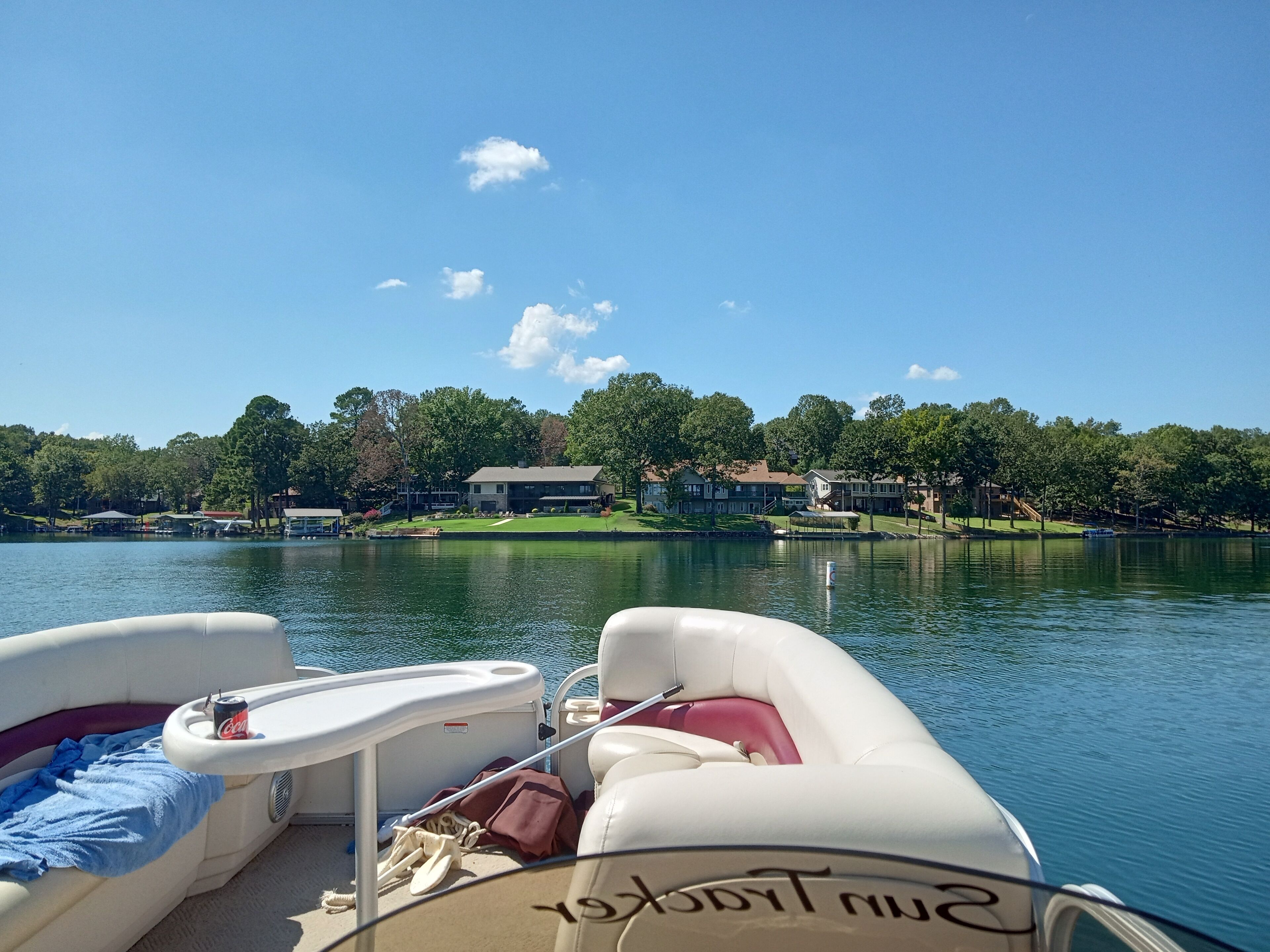 A lake view with boats docked, a clear sky, and houses in the background.