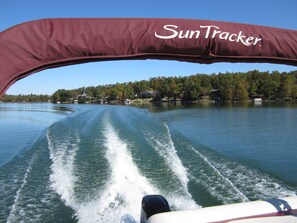 A boat with a maroon canopy labeled "Sun Tracker" moving across a lake with houses and trees in the background. - Lake and boat life!
Lake Rental in a dead-end street. (Cherokee Village)