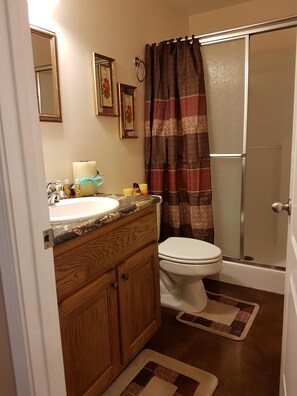 Un baño con tocador de madera, lavamanos blanco, inodoro y ducha con puerta de vidrio.