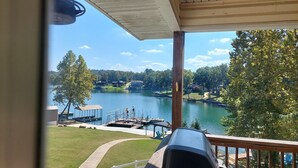 Une vue sur le lac depuis une terrasse couverte, équipée d’un barbecue et bordée d’une clôture blanche.