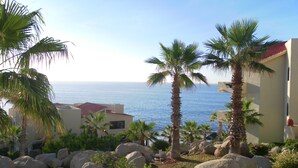A coastal view with palm trees, a building with a red roof, and the sea in the background. - New Owner Special! - 2br/2ba - Oceanview/private Beach (Cabo San Lucas)