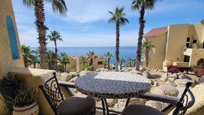 A patio with a round table and two chairs, overlooking a beach with palm trees and a clear sky. - New Owner Special! - 2br/2ba - Oceanview/private Beach (Cabo San Lucas)
