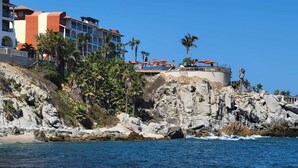 A coastal hotel with a rocky shoreline, palm trees, and a clear blue sky. - New Owner Special! - 2br/2ba - Oceanview/private Beach (Cabo San Lucas)