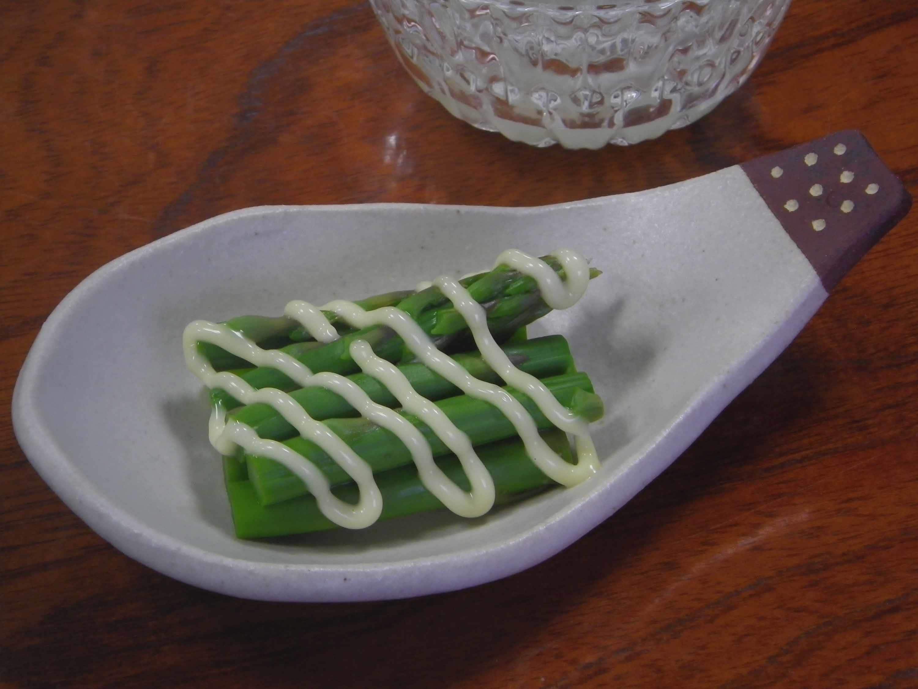 A white ceramic spoon with a purple handle containing green vegetables and a white sauce.
