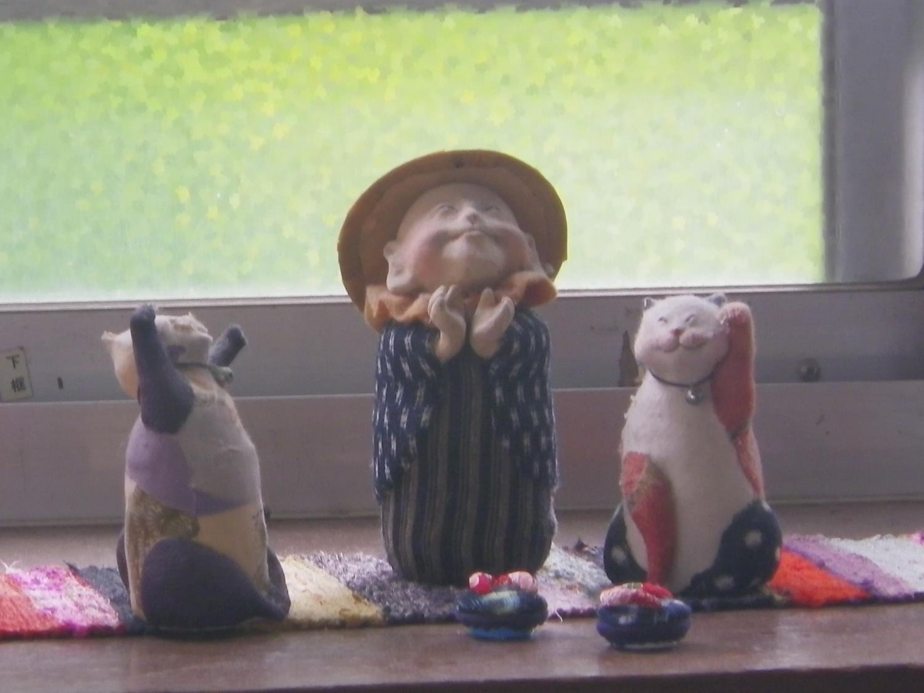 Three ceramic figurines on a windowsill with a view of a green field.