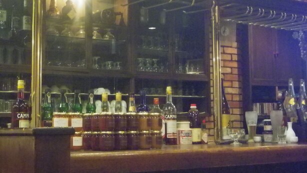Uma área de bar com prateleiras repletas de garrafas e copos diversos.