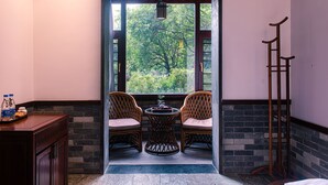 A room with two wicker chairs, a small round table, a wooden sideboard, and a view of greenery through a window. - Aroma Tea House (Guilin)