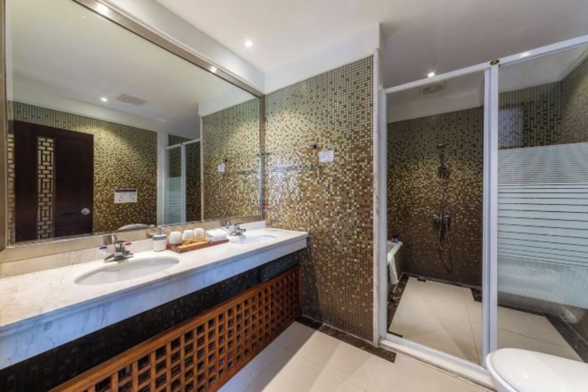 A modern bathroom with a large mirror, two sinks, a shower enclosure, and a toilet.