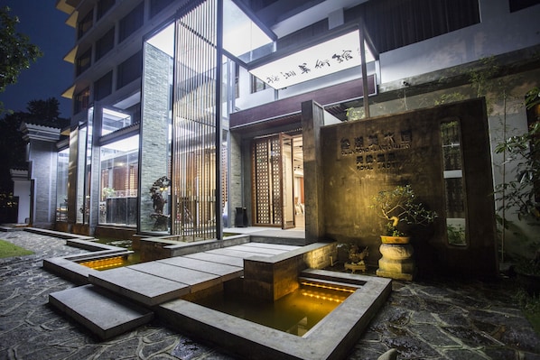 Un edificio moderno con estilo arquitectónico chino tradicional, que presenta un patio con fuente de agua y escalones de piedra.