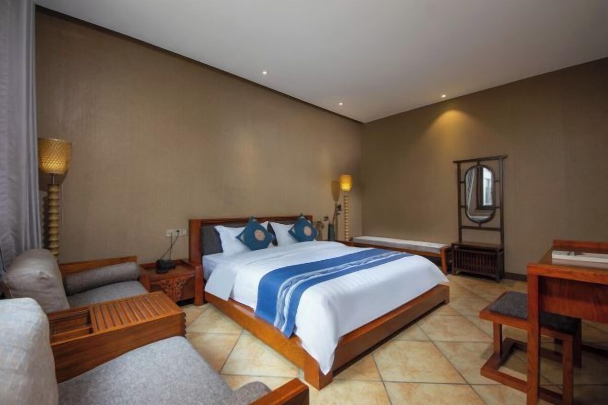 A hotel room with a large bed, a sofa, a wooden coffee table, a desk, and a lamp.