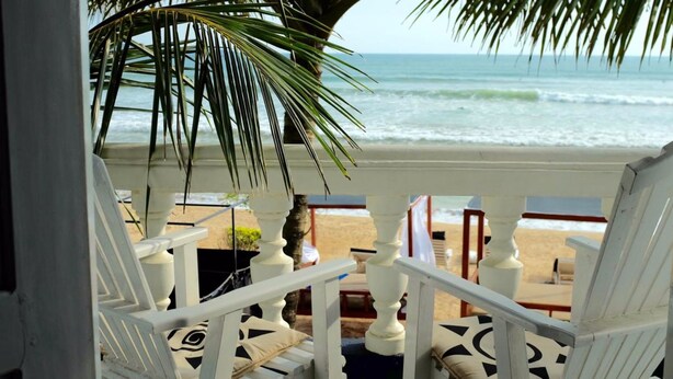 A beach view from a porch with white railings and a palm tree. - Neptune Story Hotel (Weligama)