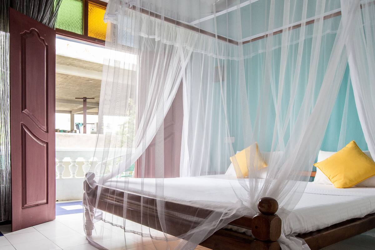 A room with a bed under a mosquito net, a wooden headboard, and a view of the outside balcony.