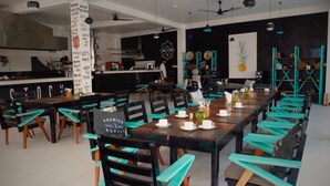 A restaurant with a long communal table, chairs, and a bar area. - Neptune Story Hotel (Weligama)