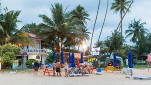 A beachside hotel with outdoor seating, palm trees, and a sign for 'Neptune Story'. - Neptune Story Hotel (Weligama)
