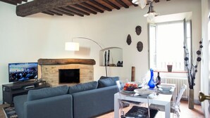Ein Wohnzimmer mit Kamin aus Stein, einer Couch, einem Fernseher und einem Essbereich mit Tisch für zwei Personen.