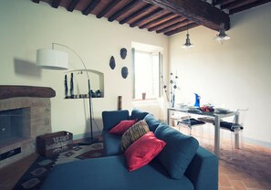 A living room with a blue sofa, red cushions, a standing lamp, and a brick fireplace. - La Senesina, Monteriggioni, Siena. In the best countryside of Tuscany ! (Siena)