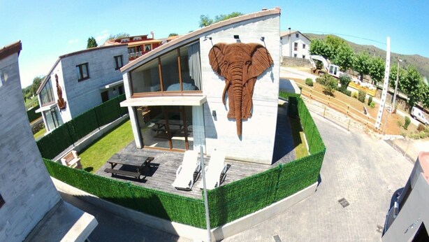Ein modernes Haus mit einem großen Elefanten-Wandbild an der Fassade, einer überdachten Terrasse und einem gepflegten Rasen.