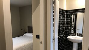 Ein Hotelzimmer mit einem Bett, einem Nachttisch, einer Wandleuchte, einer schwarz-weißen Fliesenwand und einem weißen Waschbecken.
