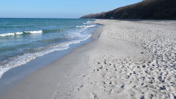 Une plage avec des empreintes de pas dans le sable et un ciel dégagé.