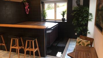 Une cuisine moderne dotée d’un îlot central, de tabourets de bar, d’une table à manger avec des chaises et de plantes en pot.