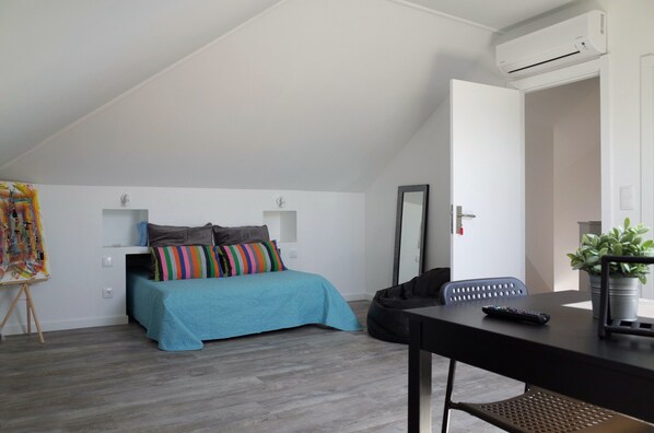 A bedroom with a bed, a desk, a chair, an air conditioner, and a potted plant. - Lisbon Beach Apartments 6. Studio, beach 5 minutes, free wifi. (Costa da Caparica)