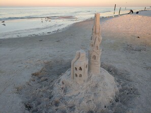 A sandcastle with a tower and arched windows on a beach.