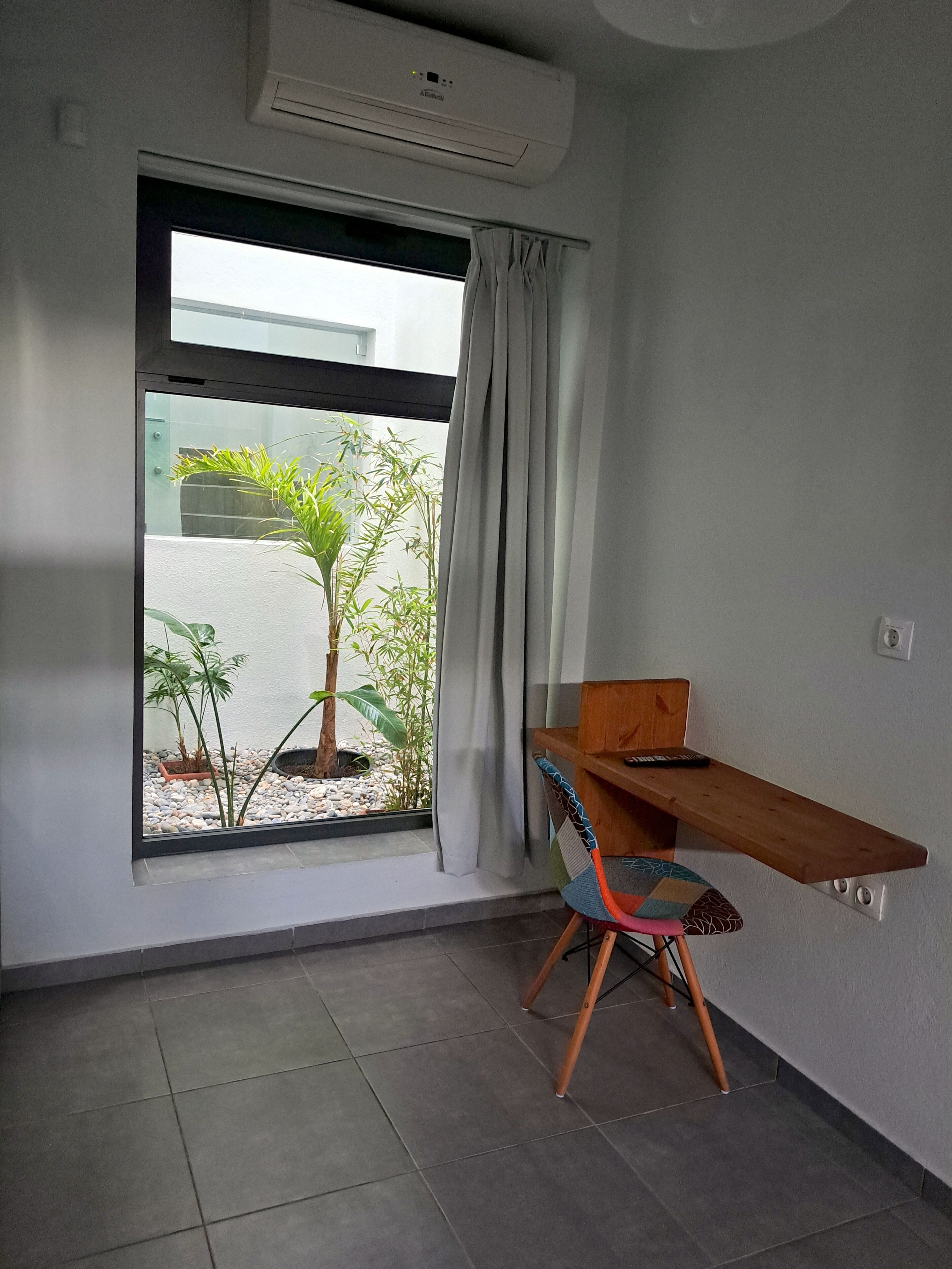 A room with a large window, a wooden desk, a chair, and a small potted plant.