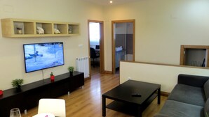 A living room with a flat-screen TV, a black coffee table, a grey sofa, and a dining area with a table set for two. - Quiet apartment in the geographical center of the Basque Country (Mendaro)