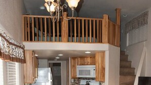Una cocina amplia con armarios de madera, un comedor con mesa y sillas, una escalera que lleva a un nivel superior y un televisor sobre un mueble.