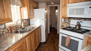 Una cocina con armarios de madera, un lavamanos de acero inoxidable, un refrigerador blanco, una estufa blanca y un microondas.