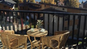 Un balcon doté de meubles en osier et d’une table, offrant une vue sur un paysage montagneux parsemé de bâtiments traditionnels.