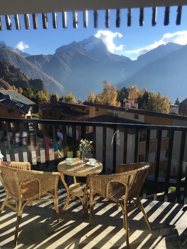 A balcony with wicker furniture and a table, overlooking a mountainous landscape.