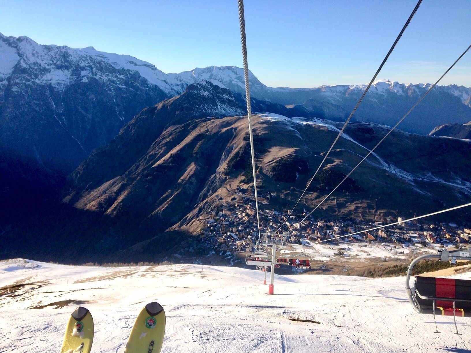 A ski lift chair with a view of a snow-covered mountain and a town below.