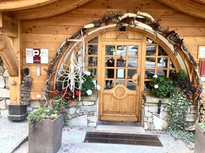 A wooden building with a large arched entrance, a stone wall, and a wooden door.