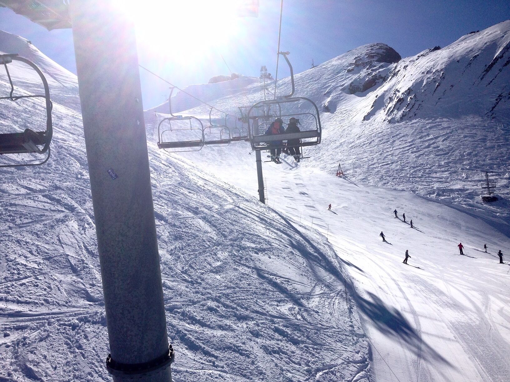 A ski lift chair moving along a snowy slope with skiers below.