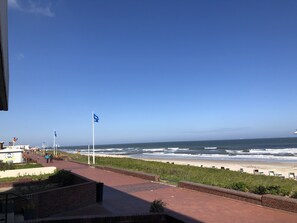 A coastal walkway with a view of the ocean, benches, and flags.