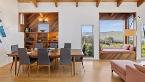 A modern dining area with a wooden table and chairs, a built-in bookshelf, and a large window offering a scenic view. - A Sanctuary to Relax and Refresh all your Senses (Inverness)