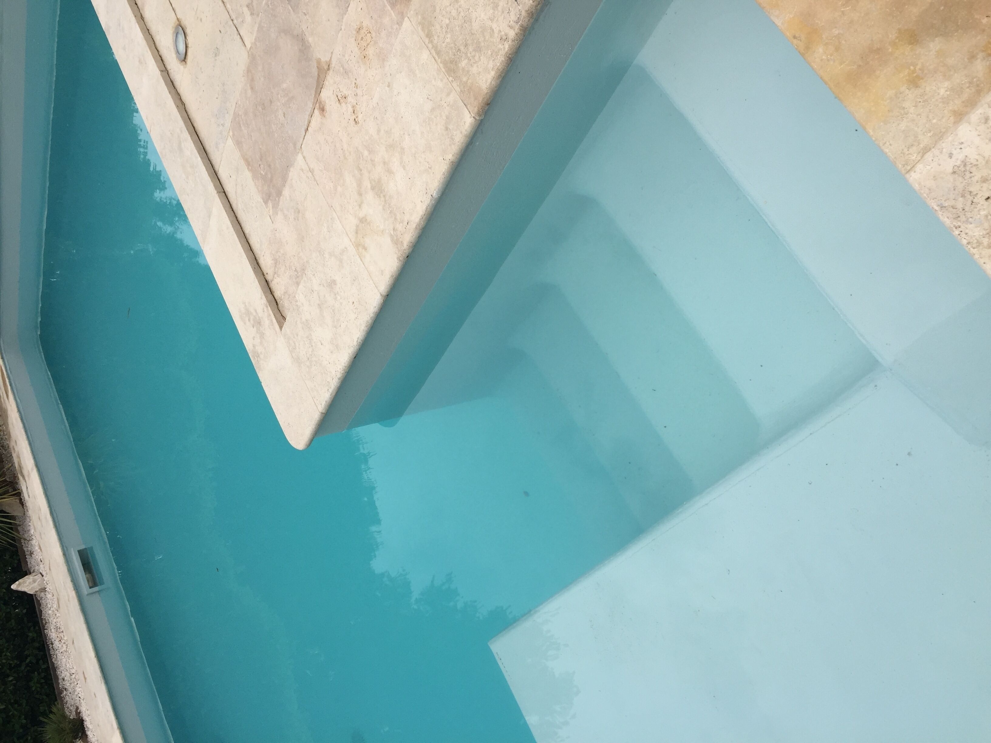Una esquina de piscina con interior azul claro y borde de azulejos blancos.